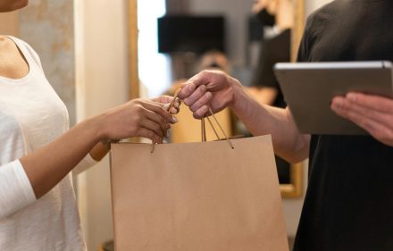 pexels-photo-6969962-6969962 Close-up of hands exchanging a shopping bag indoors, symbolizing modern retail and technology.
